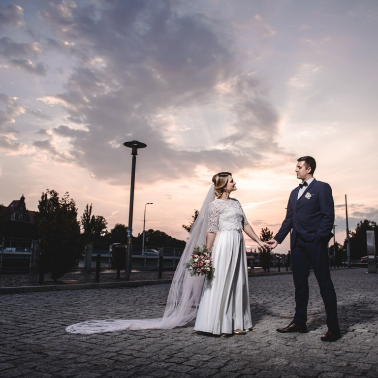 Picturesque wedding photoshoot with grey skies at dusk, bride and groom holding hands and looking into each other's eyes romantically