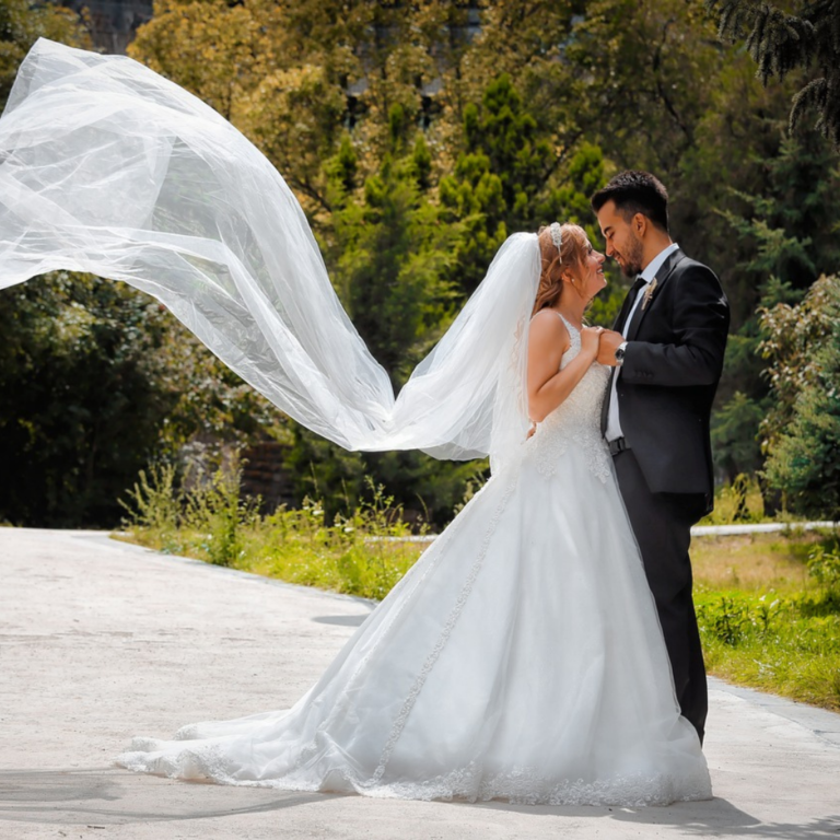 Wedding photoshoot with bride and groom holding each other, looking into each other's eyes and the bride's veil flying in the wind