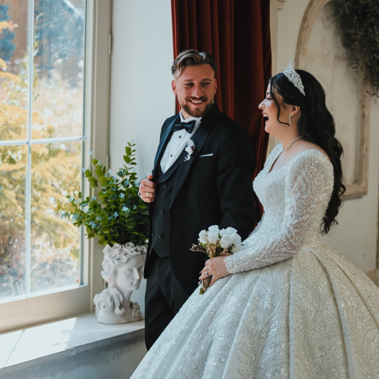 Wedding photoshoot with bride and groom holding each other, laughing and looking out of the window