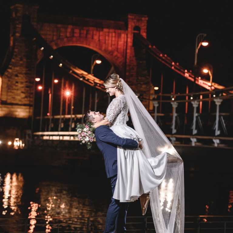 Picturesque wedding photoshoot at night, groom lifting up the bride as she wraps her arms around his neck while they're looking into each other's eyes romantically