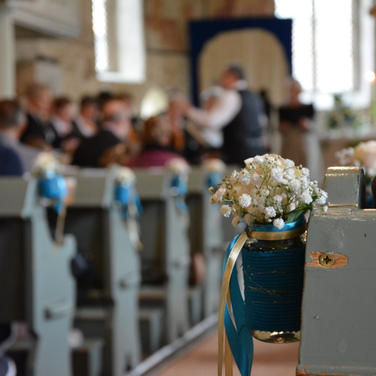 Wedding flower decoration on a pew with wedding guests blurred in the background