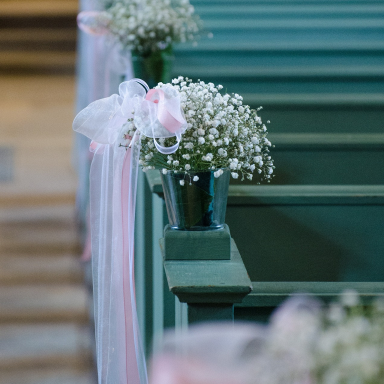 Wedding flower decoration on a pew with rows of other pews blurred in the background