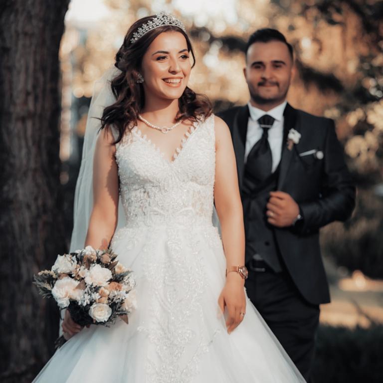 Wedding photoshoot with the bride smiling and the groom blurred in the background as he looks at the bride in front of him