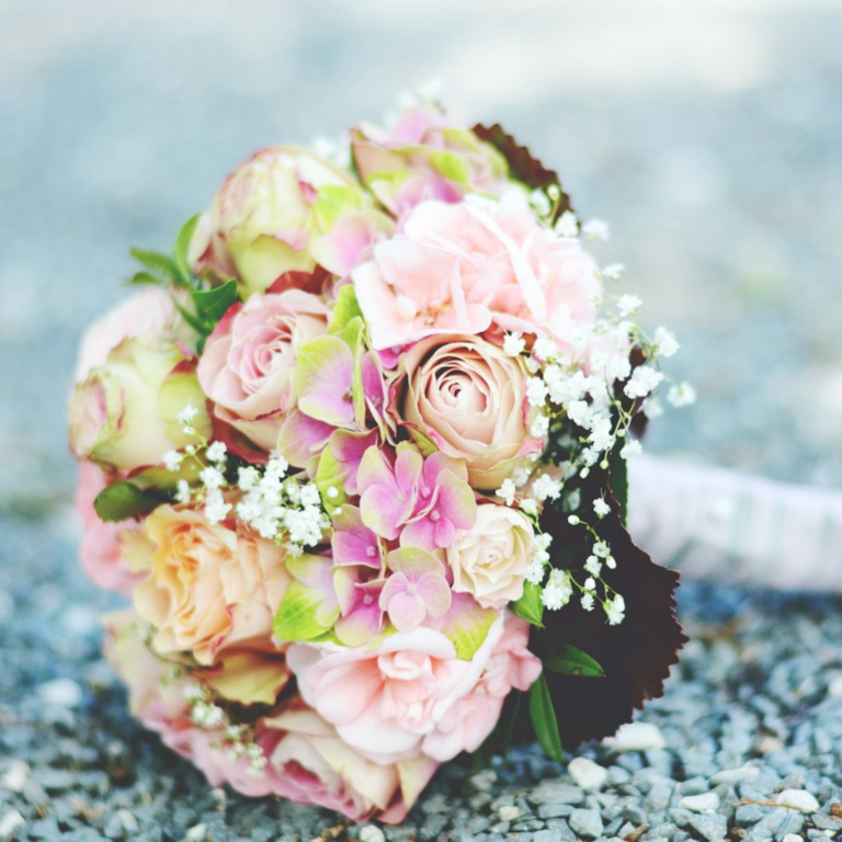 Wedding bouquet of peach roses, and other flower arrangements, laid down on a granite floor.