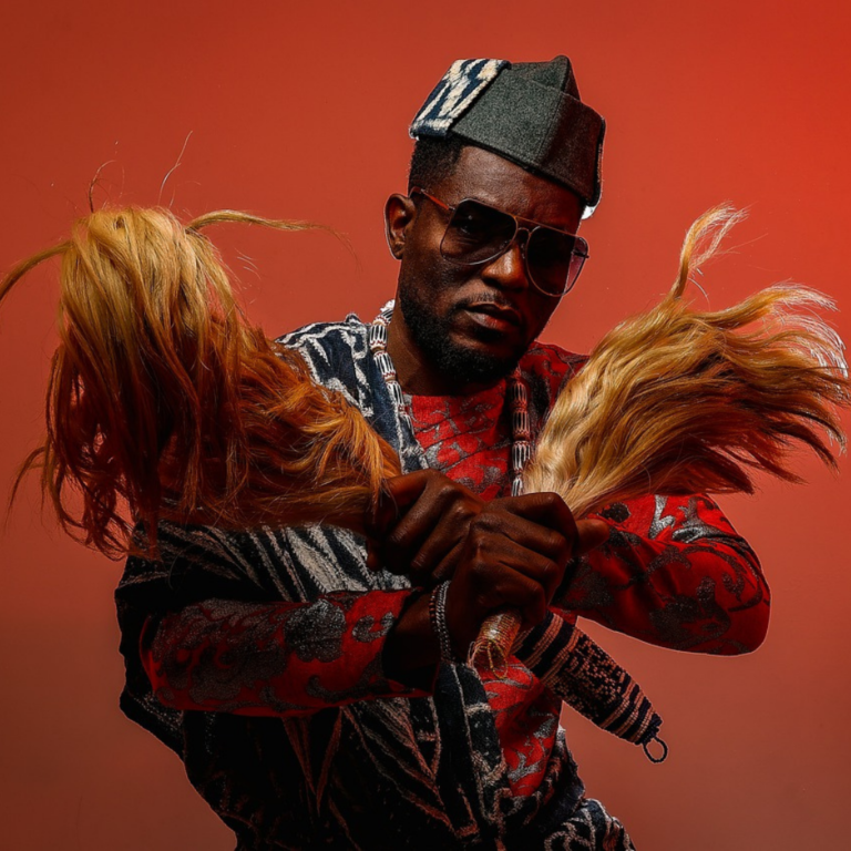 Studio portrait of a man dressed in traditional African attire and holding two horsetails