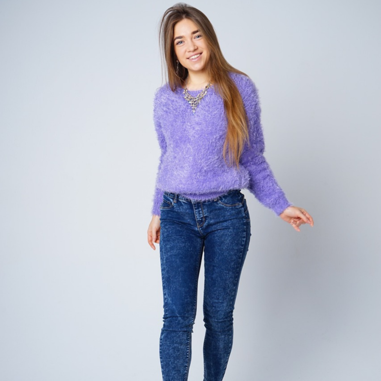 Personal studio portrait of a lady in jeans and a purple sweater, smiling and posing for the camera