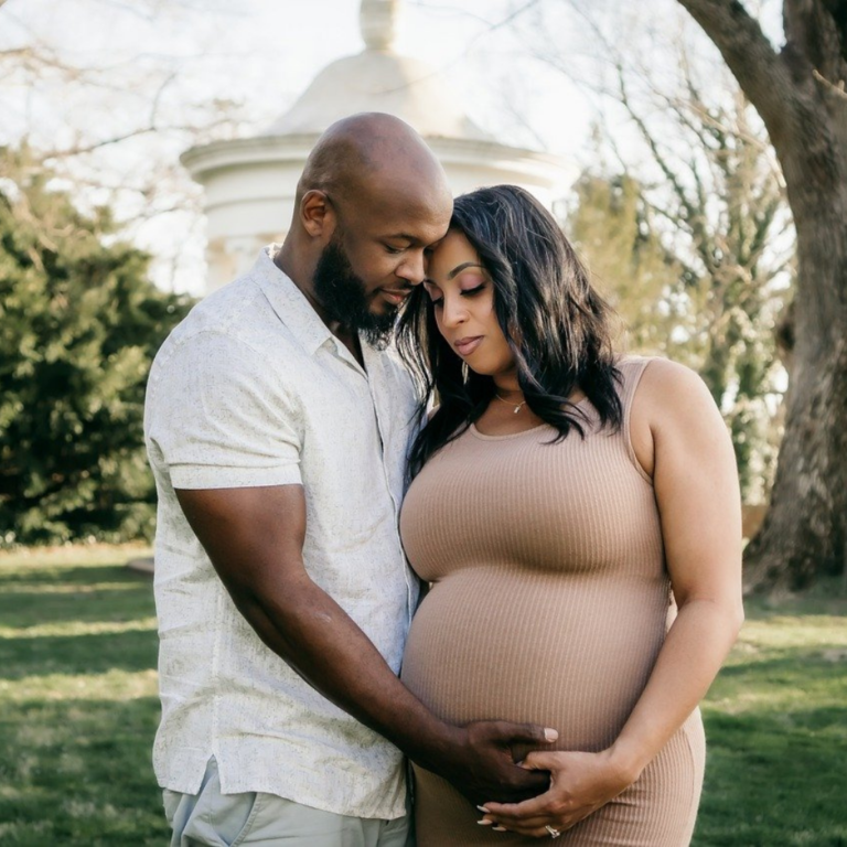 Maternity photoshoot for a couple, the husband is holding the wife's protruding belly, both of them in a warm embrace