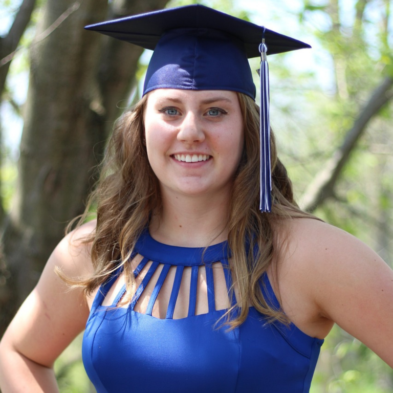 Graduation photoshoot by Quintessence Photography UK. The graduand is wearing a blue graduate cap, and a matching blue dress, happy and smiling