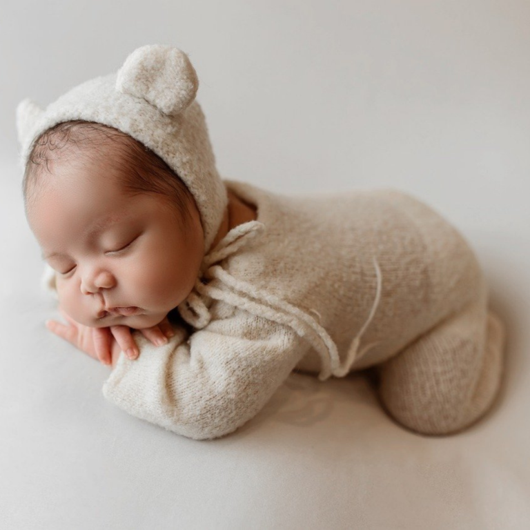 Studio photoshoot by Quintessence Photography for a cute little sleeping baby in a onesie and a head warmer cap