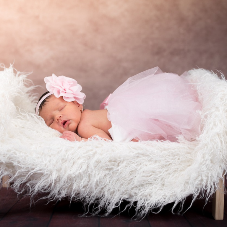 Studio photoshoot for a sleeping little child wearing a flower head bonnet and laying on a furry bed