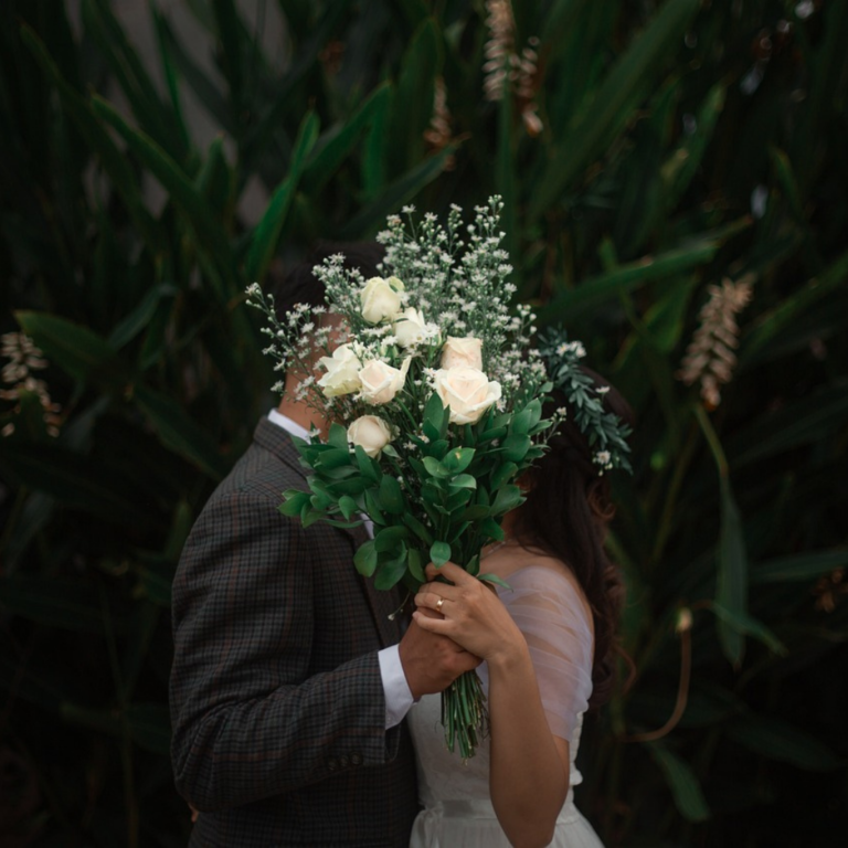 Romantic Wedding Couple kissing behind a bridal bouquet of white roses